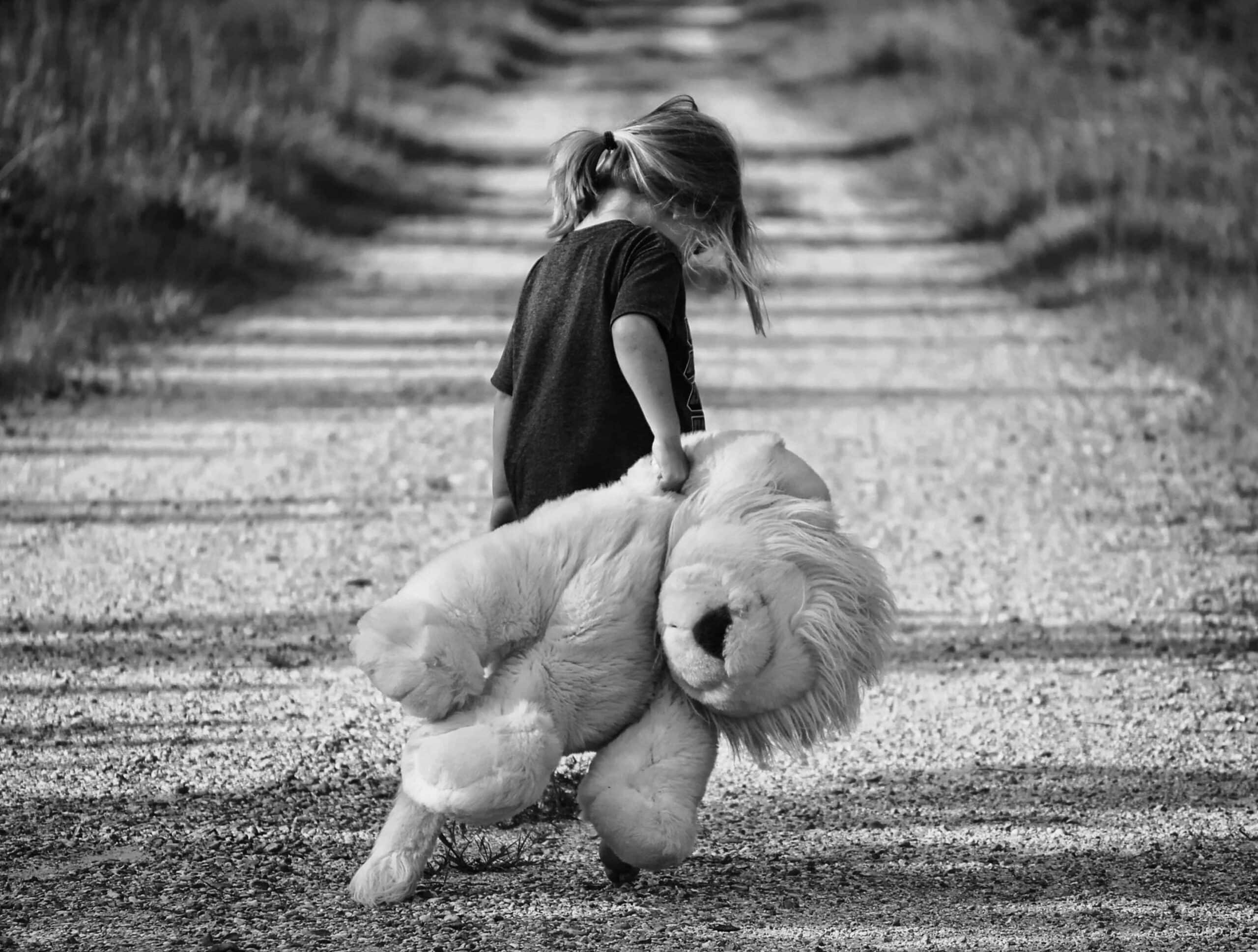 Grayscale image of child dragging stuffed animal down a gravel path.